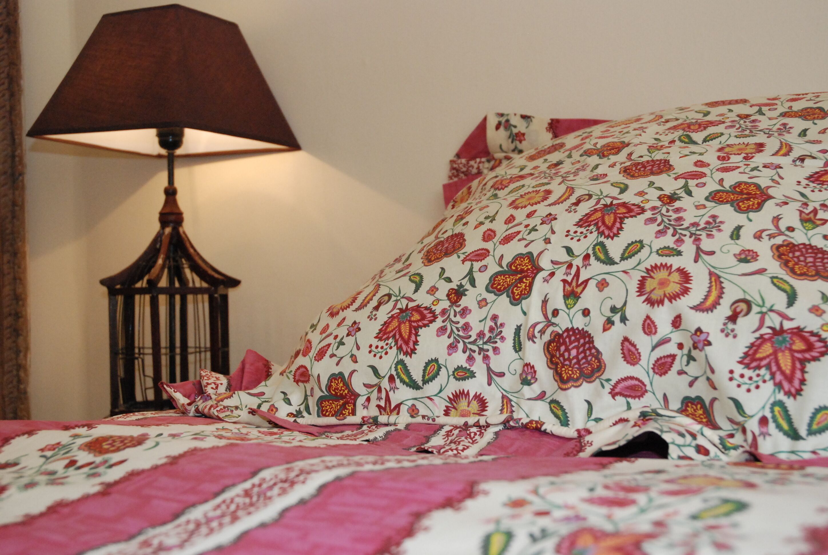 Un lit avec une literie à motifs floraux, une lampe de couleur sombre et un coussin décoratif à motifs.