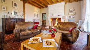 A cozy living room with two leather sofas, a wooden coffee table with plates of food, and a fireplace in the background.