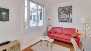 Een moderne woonkamer met een rode bank, een kleine witte tafel, een vloerlamp en een groot raam.
