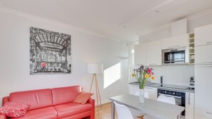 Een modern appartement met een rode bank, een eettafel, een keuken met witte kasten en een zwart-wit poster aan de muur.