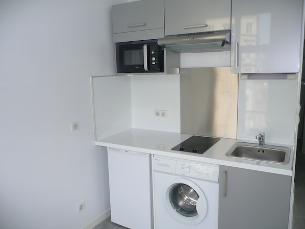 Cocina compacta equipada con microondas, estufa, fregadero y lavadora integrada.