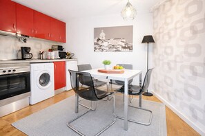 A compact kitchen with red cabinets, a washing machine, a dining table with chairs, and a pendant light.