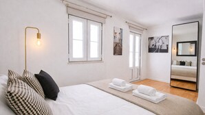 A bedroom with a large bed, a bedside lamp, a mirror, and a window.