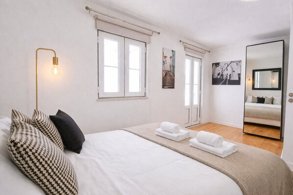A bedroom with a large bed, a bedside lamp, a mirror, and a window.