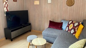 Een woonkamer met een flatscreen televisie, een grijze bank en een poef.