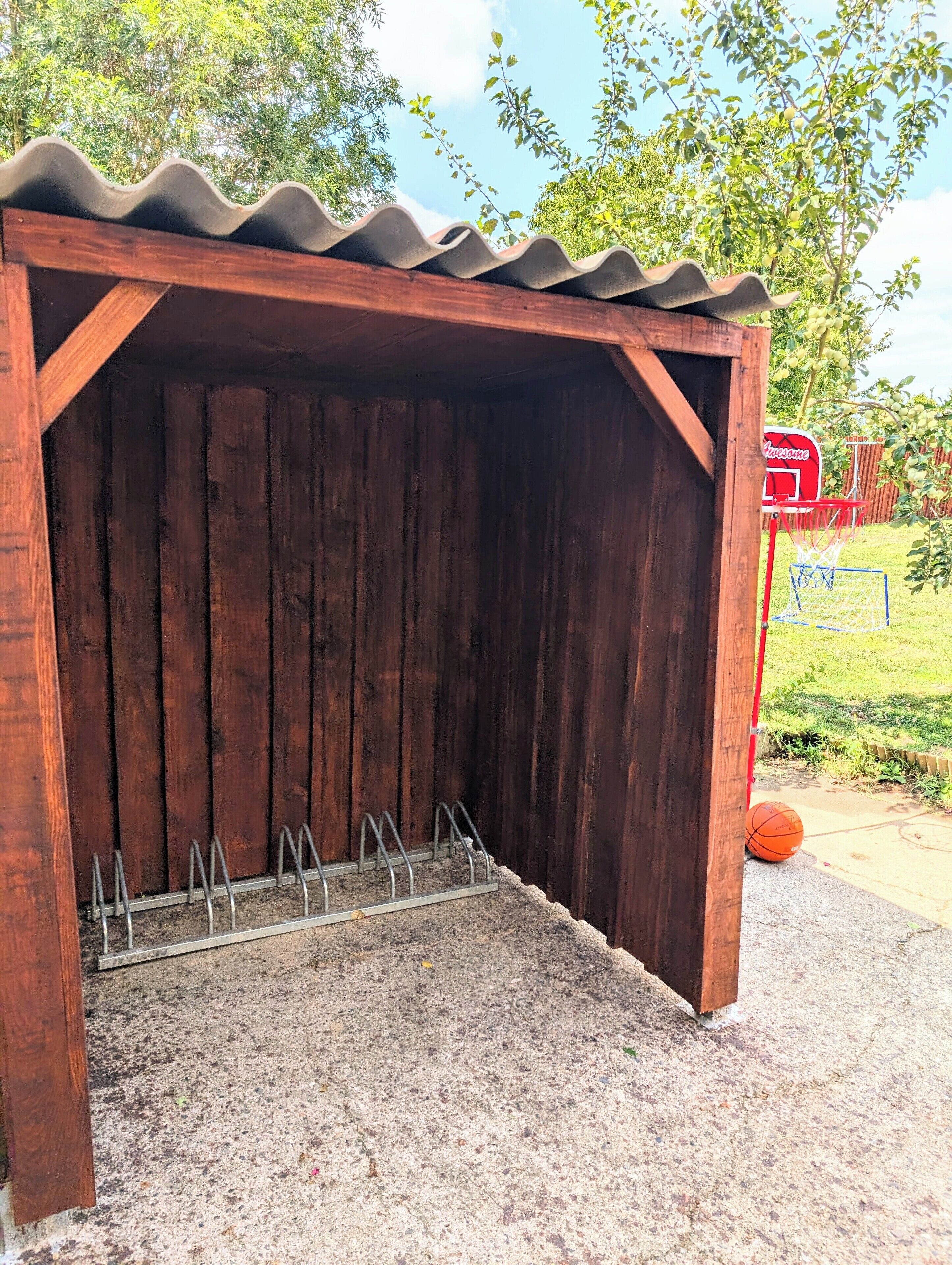 Eine Holzhütte mit Wellblechdach, einem Metallgestell und einem Basketballkorb.