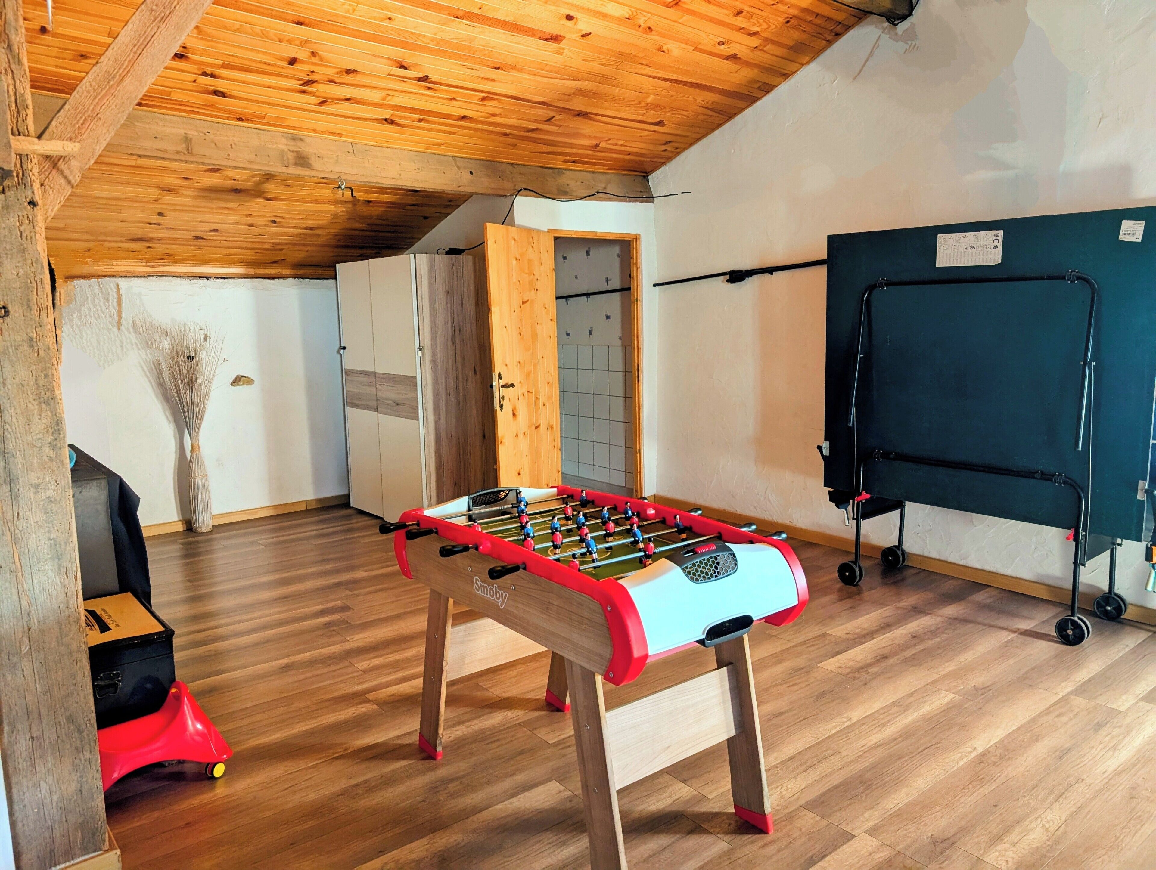 A room with a wooden ceiling, a foosball table, a small red toy car, and a whiteboard on the wall.