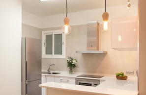 Una cocina moderna con electrodomésticos de acero inoxidable, encimera blanca e iluminación colgante.