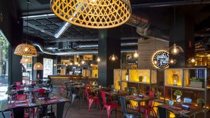 Ein Restaurantinneres mit Tischen, Stühlen, einer Bar und hängenden Pendelleuchten.