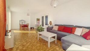 Un salon moderne avec un canapé gris, des coussins rouges, une table basse blanche et un coin repas avec une nappe rouge.