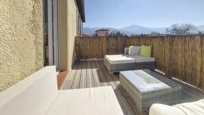 Un balcon agrémenté de meubles en osier, offrant une vue sur les montagnes et délimité par une clôture en bois.
