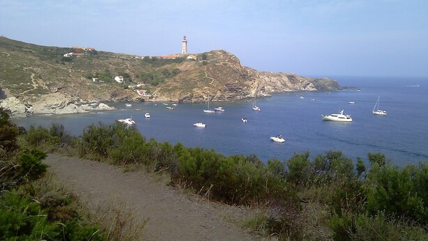 Un paysage côtier avec un phare, un terrain rocheux et plusieurs bateaux sur l’eau.