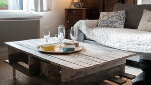 A rustic wooden table with a tray of glasses and bowls, a lamp, and a bed with patterned pillows in a cozy room with a window and wooden walls. - Fisherman's cottage in St Guénolé, near Pors Carn, La Torche (Penmarch)