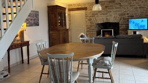 A dining area with a wooden table and chairs, a stone wall, a fireplace, and a TV. - Fisherman's cottage in St Guénolé, near Pors Carn, La Torche (Penmarch)