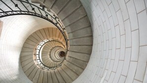 A spiral staircase with white brick walls and black metal railings. - Fisherman's cottage in St Guénolé, near Pors Carn, La Torche (Penmarch)