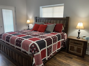 A bedroom with a wooden bed frame, a quilted bedspread, two bedside lamps, a nightstand, and a window with blinds.