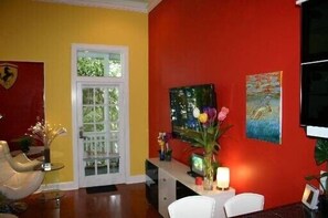 Une pièce avec un mur rouge, une porte blanche et une fenêtre. Il y a un tableau accroché au mur et un vase rempli de fleurs posé sur une table.