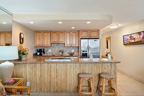 Une cuisine moderne avec des meubles en bois, un réfrigérateur en acier inoxydable et un coin bar équipé de tabourets.