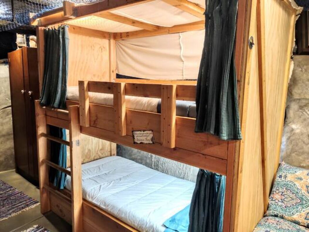 A bunk bed with a wooden frame, a lower bunk with a mattress, and a top bunk with a canopy.
