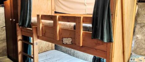 A bunk bed with a wooden frame, a lower bunk with a mattress, and a top bunk with a canopy.