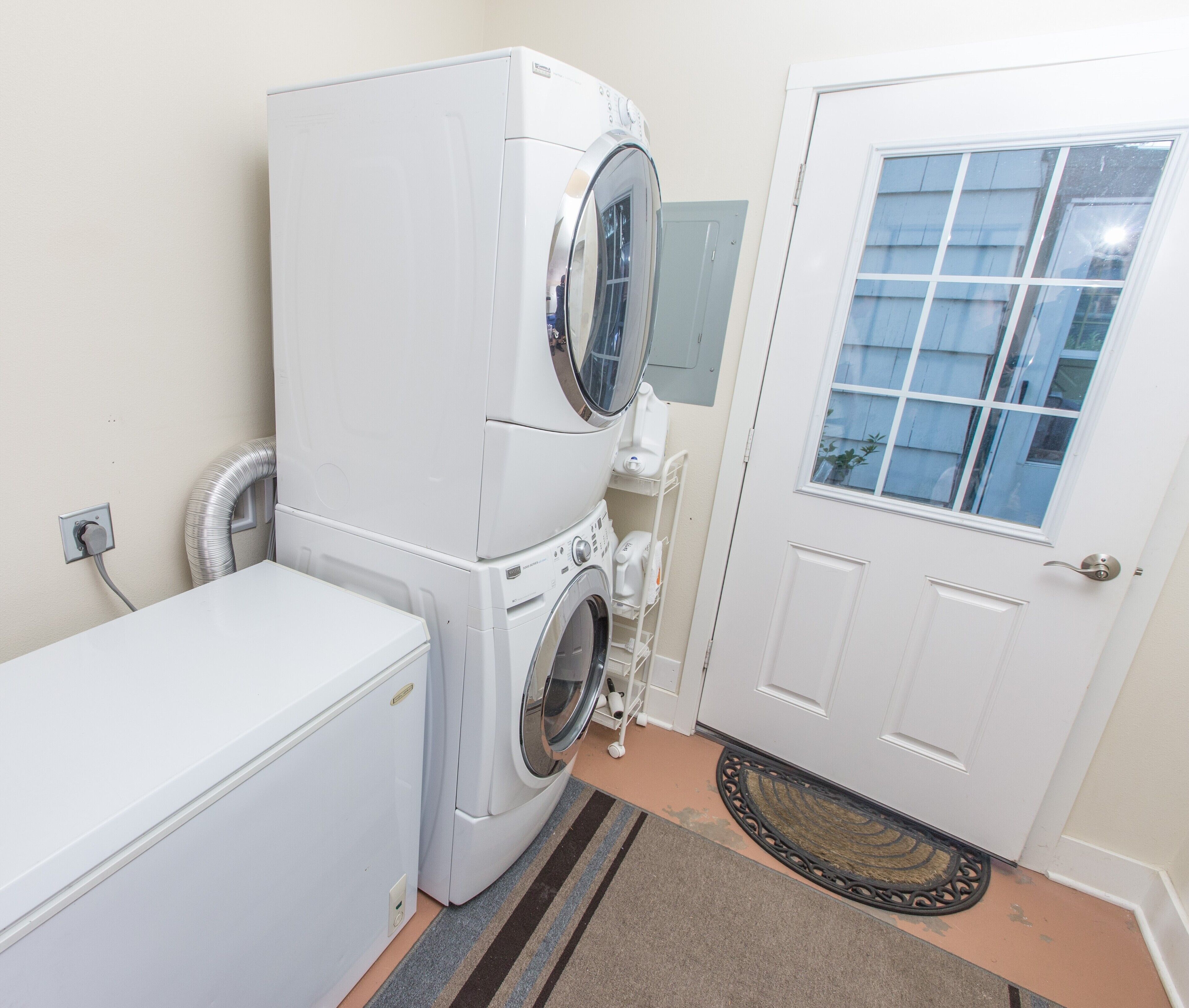 A laundry room with stacked washers and dryers, a white door, and a doormat.