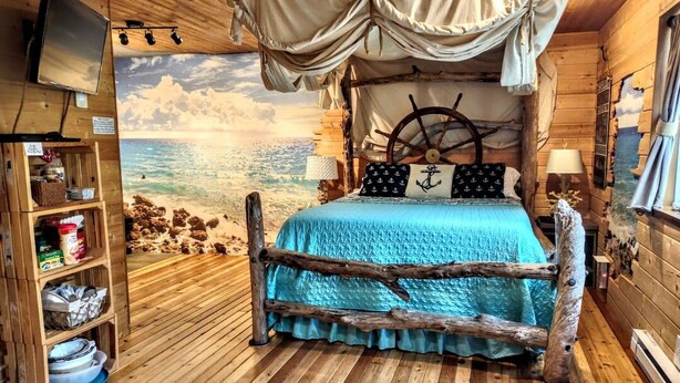 A cozy cabin-style room with a bed featuring a nautical theme, a television, and a bookshelf.