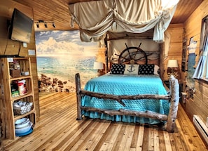 Een knus logies in een kamer met een maritiem thema, een bed, een televisie en een boekenplank.