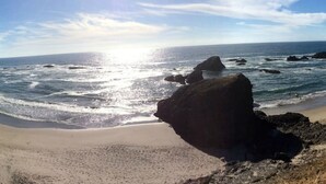 A beach with a large rock in the foreground, waves crashing onto the shore, and the ocean extending to the horizon.