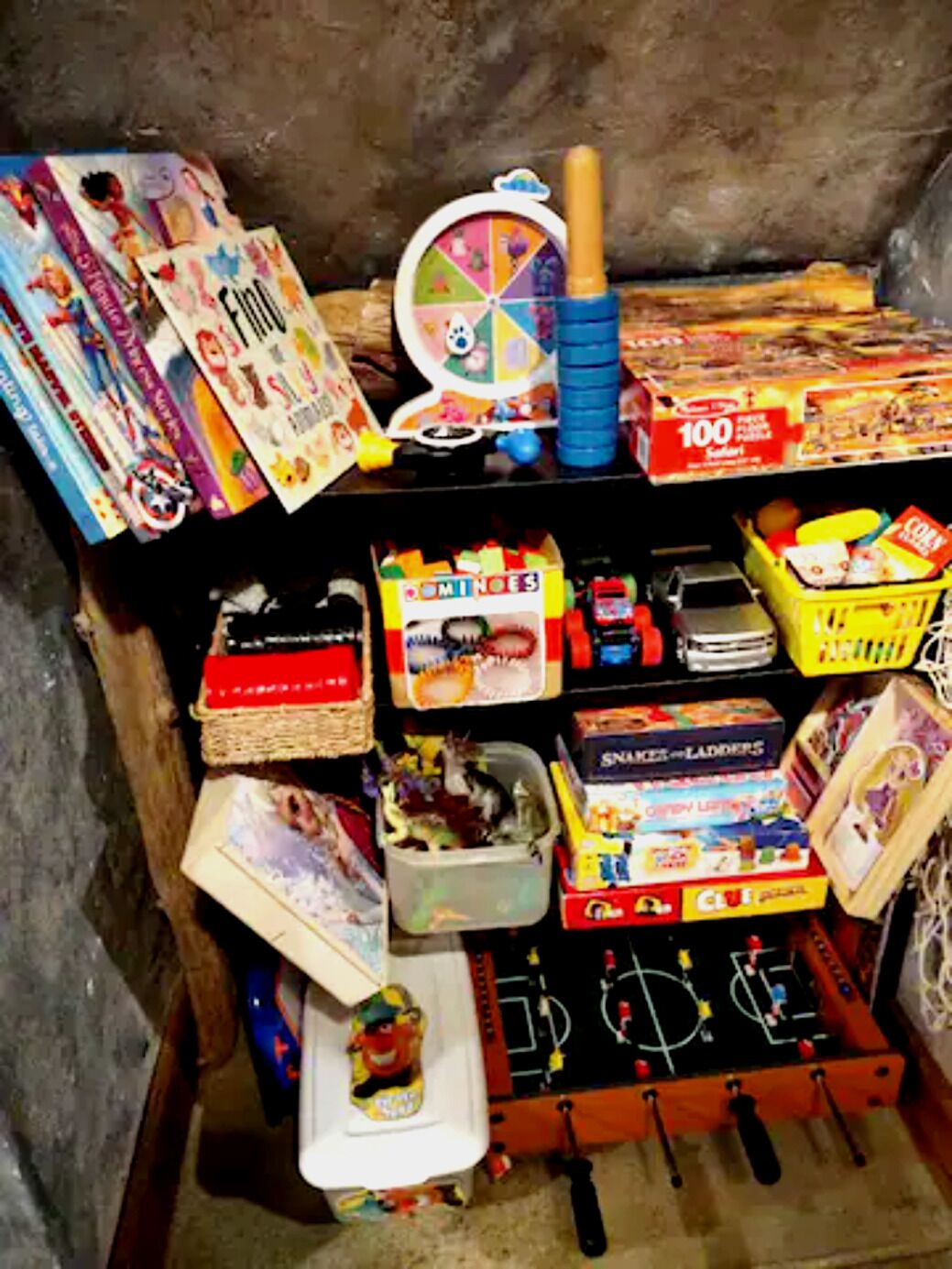Ein Stauraum mit verschiedenen Kinderspielen und -spielzeugen, darunter ein Kicker, ein Spielzeugauto und ein Puzzle.
