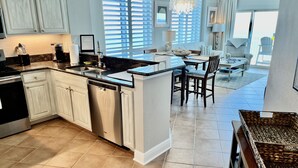 A modern kitchen with white cabinetry, a dishwasher, and a dining area with a table and chairs. - 17th Floor East Corner Unit with 2 Balconies, Huge Beachfront Pool, Low Host Fee (Gulf Shores)