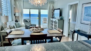 A dining area with a view of the ocean, a chandelier, and a dining table with placemats. - 17th Floor East Corner Unit with 2 Balconies, Huge Beachfront Pool, Low Host Fee (Gulf Shores)