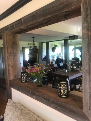 A rustic interior with a wooden beam structure, a dining table with floral centerpieces, and a chandelier.