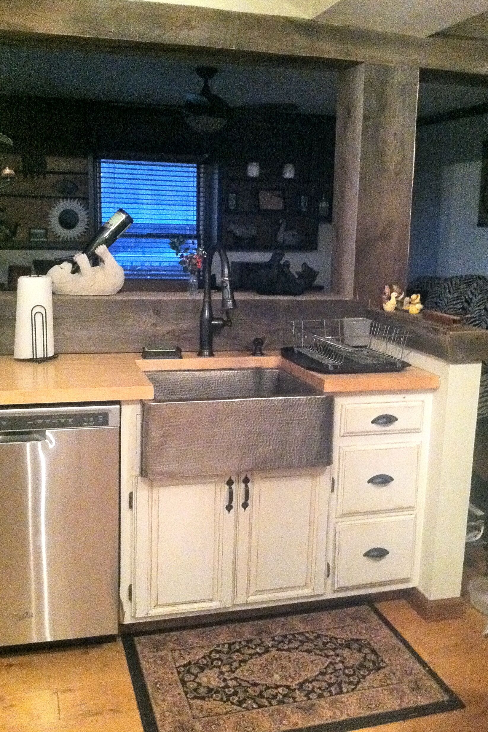A kitchen with a stainless steel dishwasher, a sink with a towel rack, and a patterned rug.