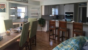 A spacious kitchen with a dining area, featuring wooden chairs, a large island, and a 'BEACHHOUSE' sign.