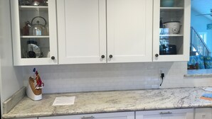 A kitchen with white cabinets, a marble countertop, and a fruit bowl.