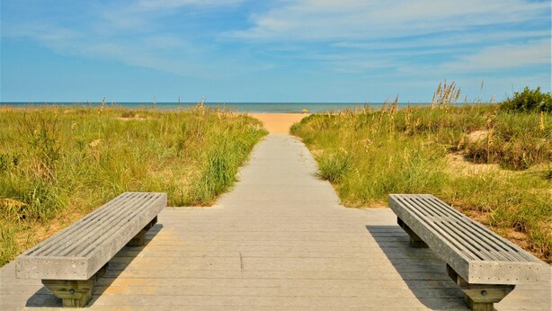 A wooden boardwalk leading to a beach with grassy dunes on either side.