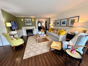 A living room with a fireplace, a television, a sofa with yellow cushions, and a coffee table.