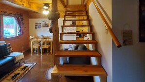 A wooden staircase leading to a second floor, with a dining area and a sofa in the foreground. - Alaska Aurora Adventures  Cabin B<br>World class Northern lights viewing (North Pole)
