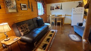 A cozy log cabin interior with a leather sofa, a dining table, and a refrigerator. - Alaska Aurora Adventures  Cabin B<br>World class Northern lights viewing (North Pole)