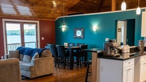 A spacious living area with a wooden ceiling, a dining table with chairs, a kitchen area with a coffee machine, and a view through a glass door. - Prime location - Ranch House on Seneca Lake (Romulus)