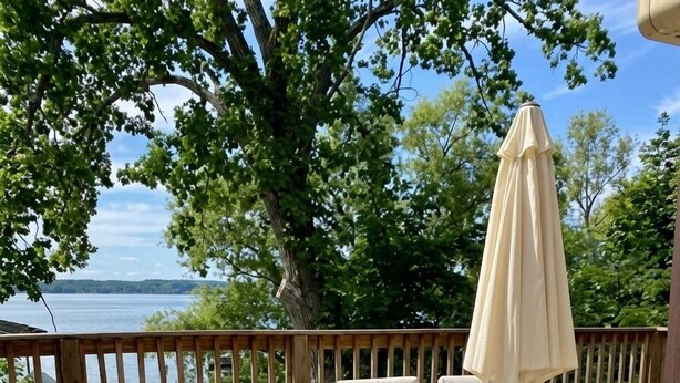 A wooden deck with outdoor furniture, a table, and chairs, overlooking a body of water. - Prime location - Ranch House on Seneca Lake (Romulus)