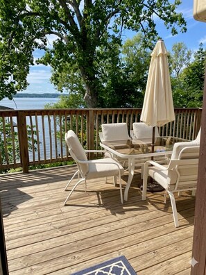 Eine Holzterrasse mit Gartenmöbeln, einem Tisch und Stühlen mit Blick auf ein Gewässer.