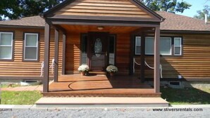 A two-story wooden house with a front porch, a door with a glass panel, and a small garden area with potted plants. - Prime location - Ranch House on Seneca Lake (Romulus)