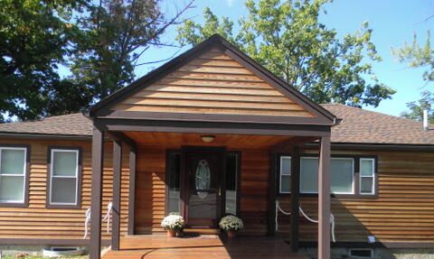A two-story wooden house with a front porch and a small front yard.