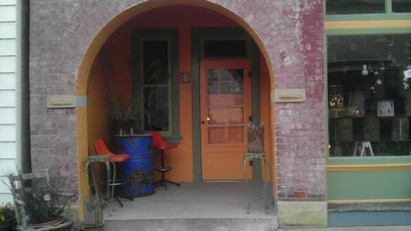 A brick building with a large arched entrance, a door, and two red chairs outside. - Downtown historic main street (Ste. Genevieve)