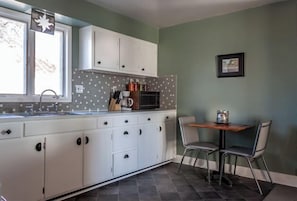 Una cocina con armarios blancos, salpicadero de azulejos, una ventana y un comedor con dos sillas.