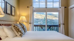 A hotel room with a bed, a nightstand, a lamp, a window with curtains, and framed pictures on the wall.