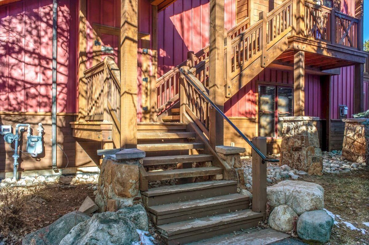 Un escalier en bois menant à un bâtiment dont la base est en pierre et qui est surmonté d’une rambarde en métal.