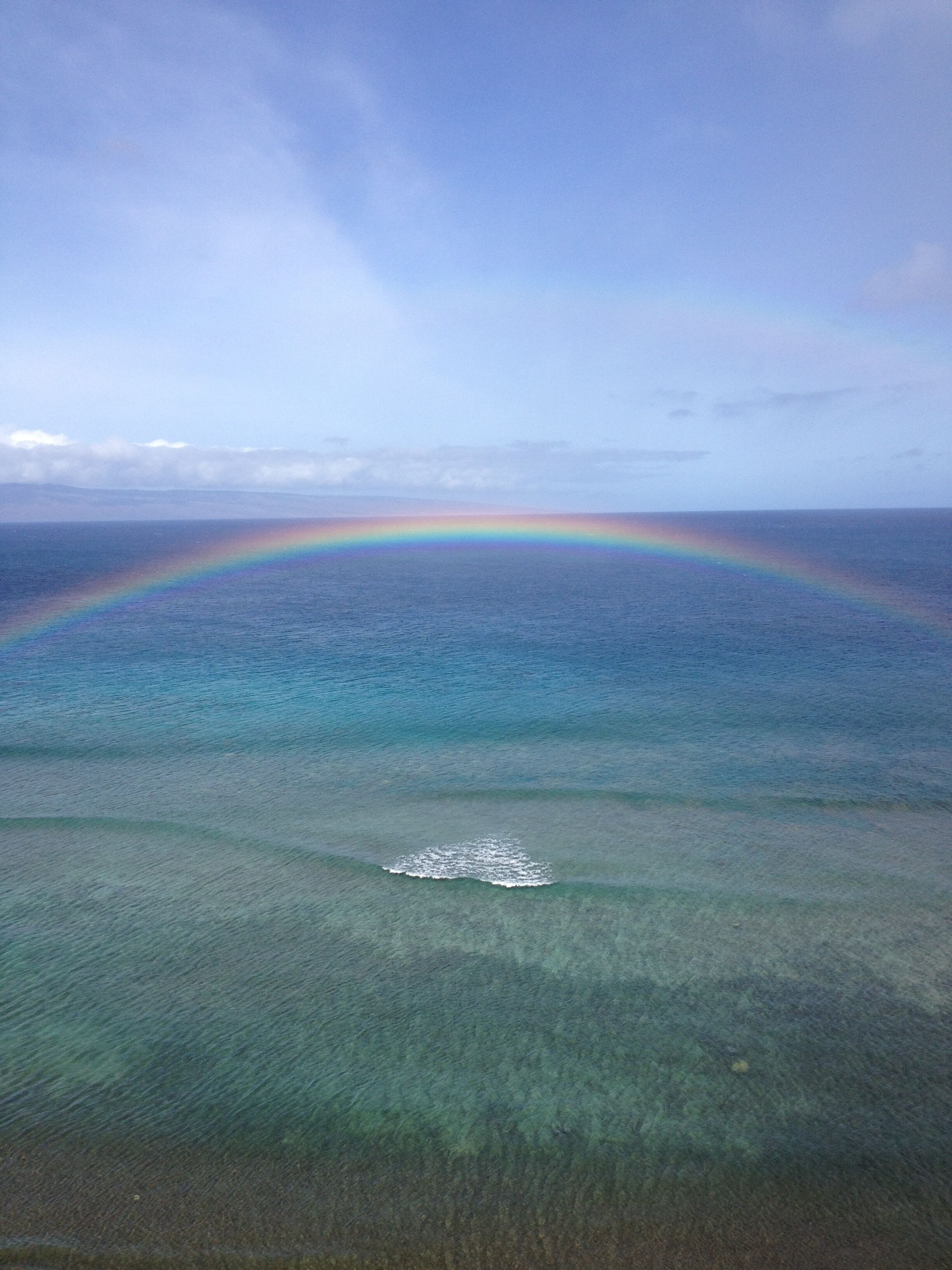 A clear view of a beach with a rainbow over the ocean.