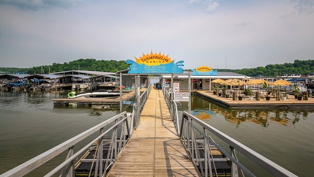A wooden pier leading to a marina with boats docked, a sign for 'Taylorsville Lake Marina', and a row of umbrellas on the dock. - Bourbon Trails, Fishing and Relaxing - Taylorsville Lake has it all! (Taylorsville)